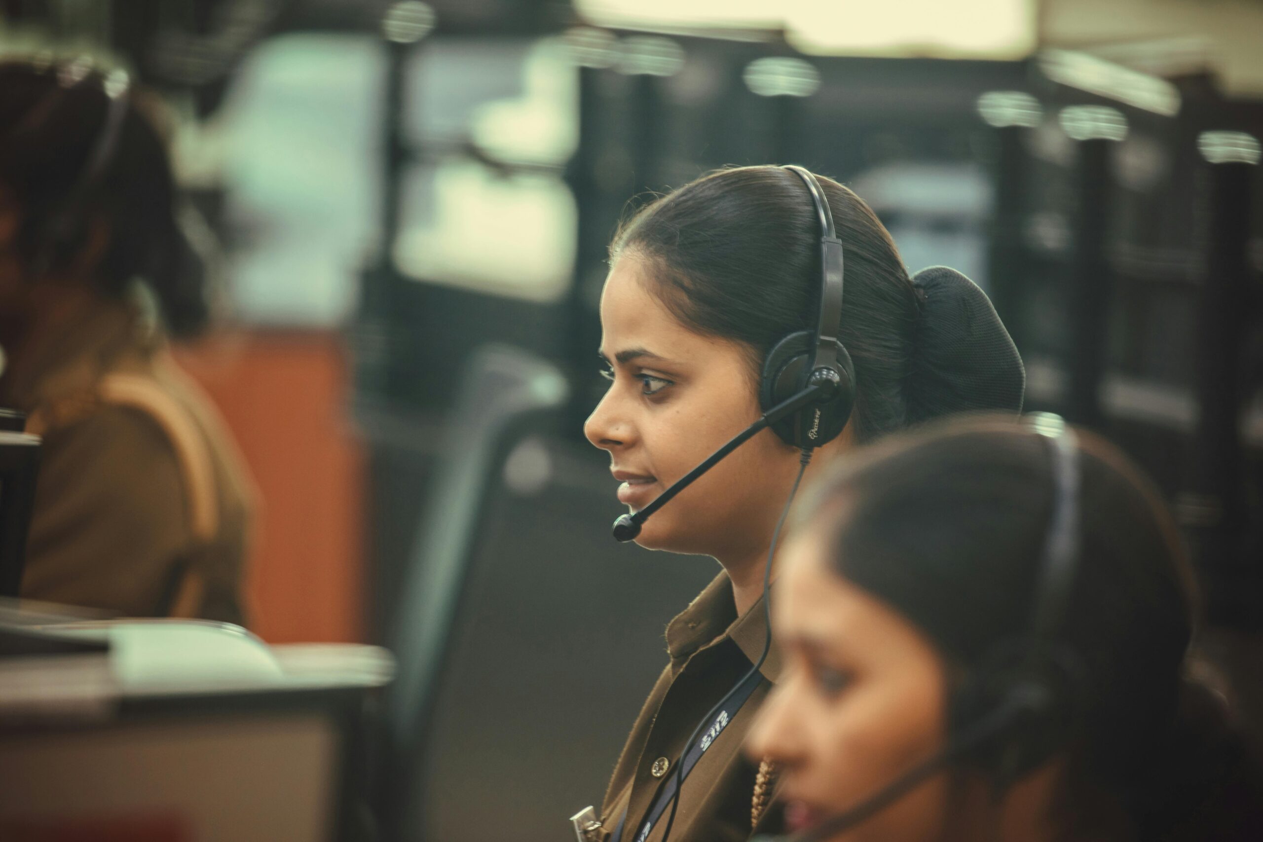 Side view of a call center agent wearing a headset, working diligently in a busy office environment.