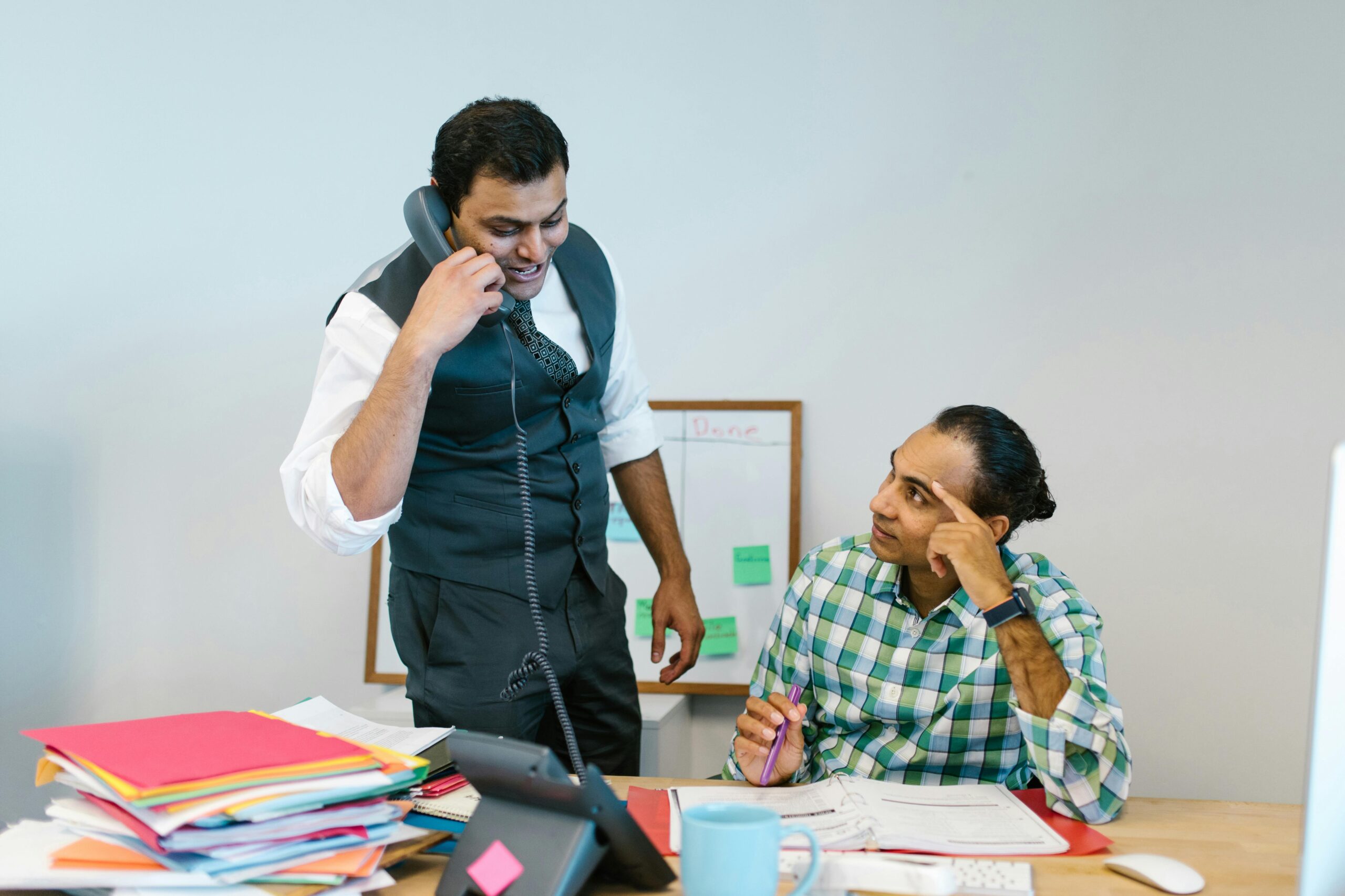 Two male colleagues collaborating in office, one talking on phone